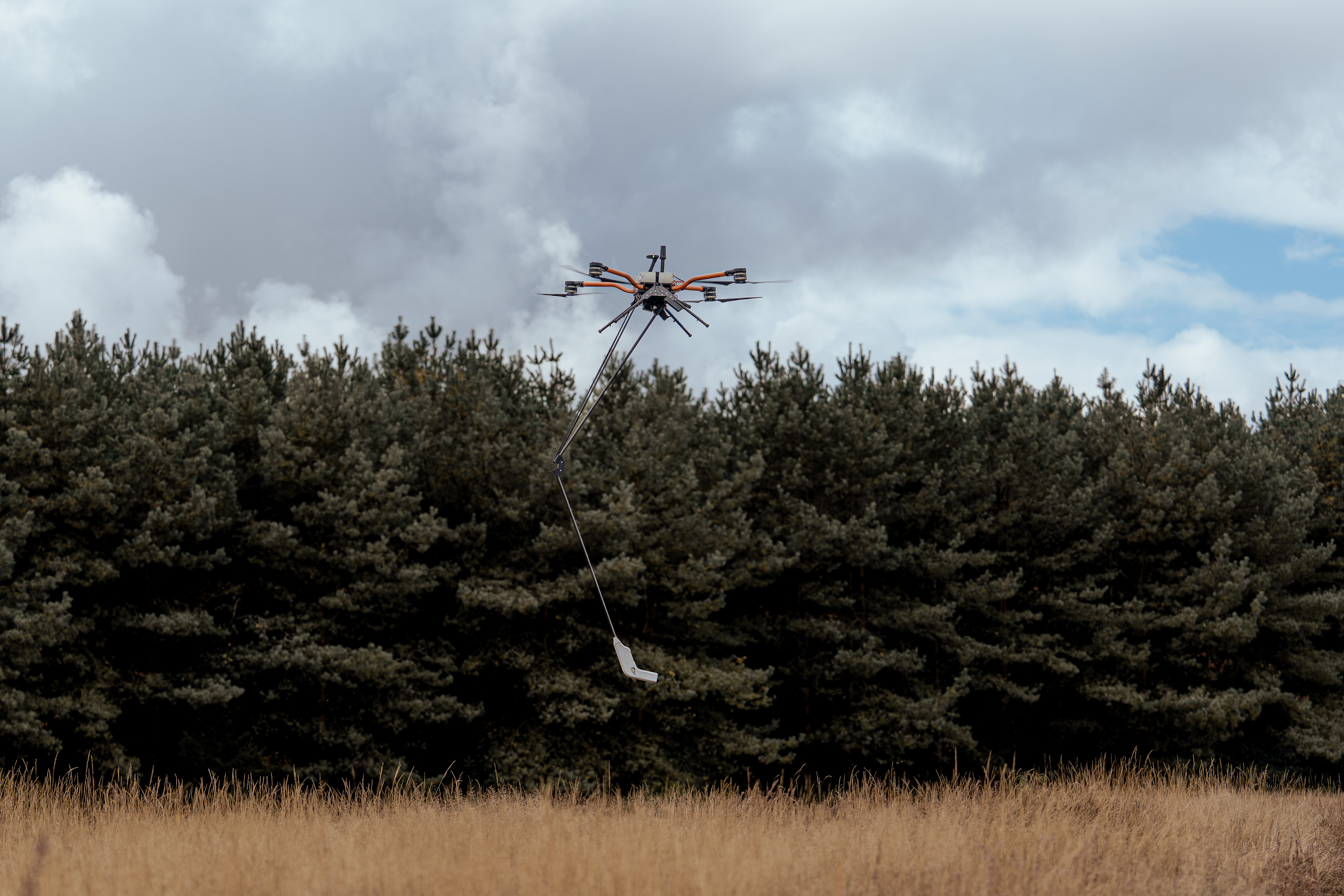 Minesweeper drone in flight carrying sensor payload over field terrain